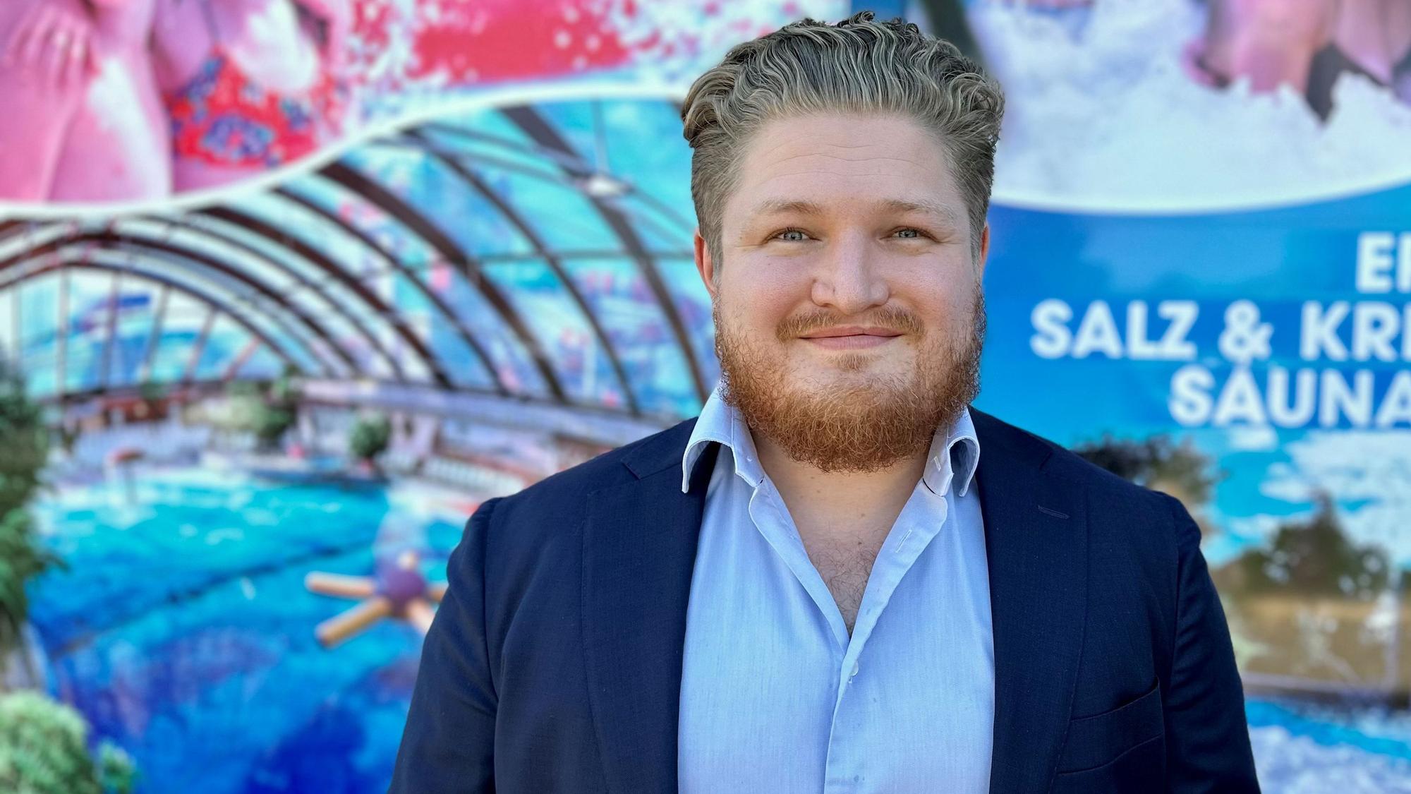 Nicolas Steinhart, Mitglied der Geschäftsleitung des Freizeitbads Aqualand in Köln-Chorweiler, steht vor einer Plakatwand.