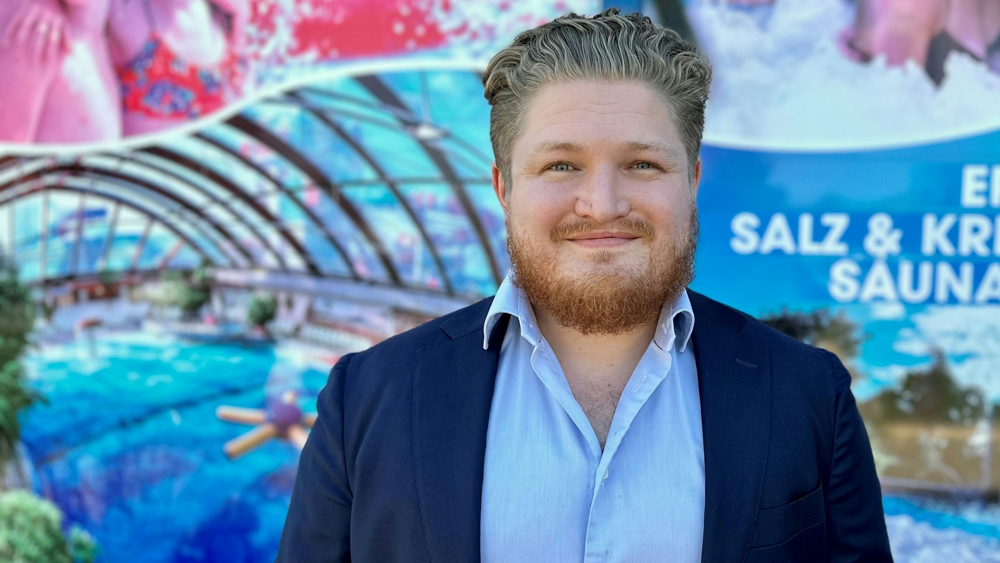 Nicolas Steinhart, Mitglied der Geschäftsleitung des Freizeitbads Aqualand in Köln-Chorweiler, steht vor einer Plakatwand.