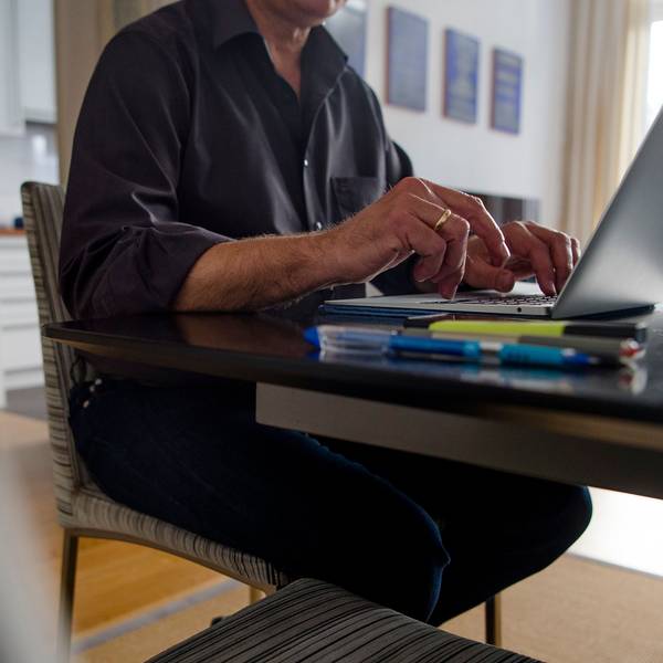 Ein Mann sitzt zuhause an einem Esstisch und arbeitet an einem Laptop.