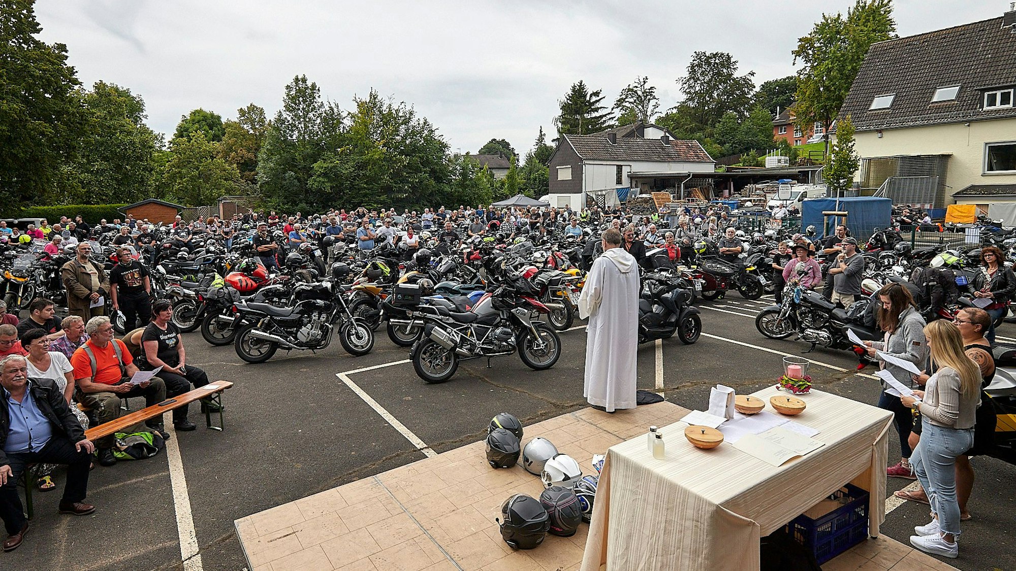 Pfarrer Hardy Hawinkels steht auf einer kleinen Bühne auf dem Asphalt vor einem Altar. Um ihn herum stehen viele Motorräder. Auf Bänken sitzen ihre Besitzer.