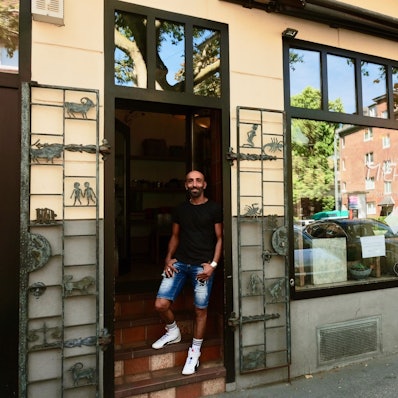 Ein Mann mit dunklem T-Shirt und kurzer Jeans steht im Eingang eines Ladenlokals.