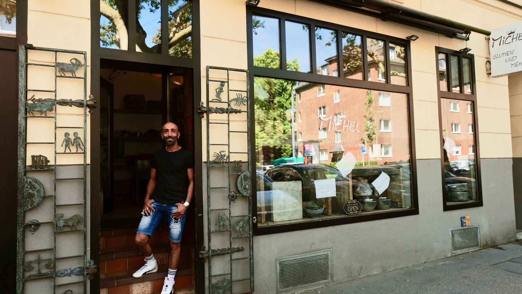 Ein Mann mit dunklem T-Shirt und kurzer Jeans steht im Eingang eines Ladenlokals.