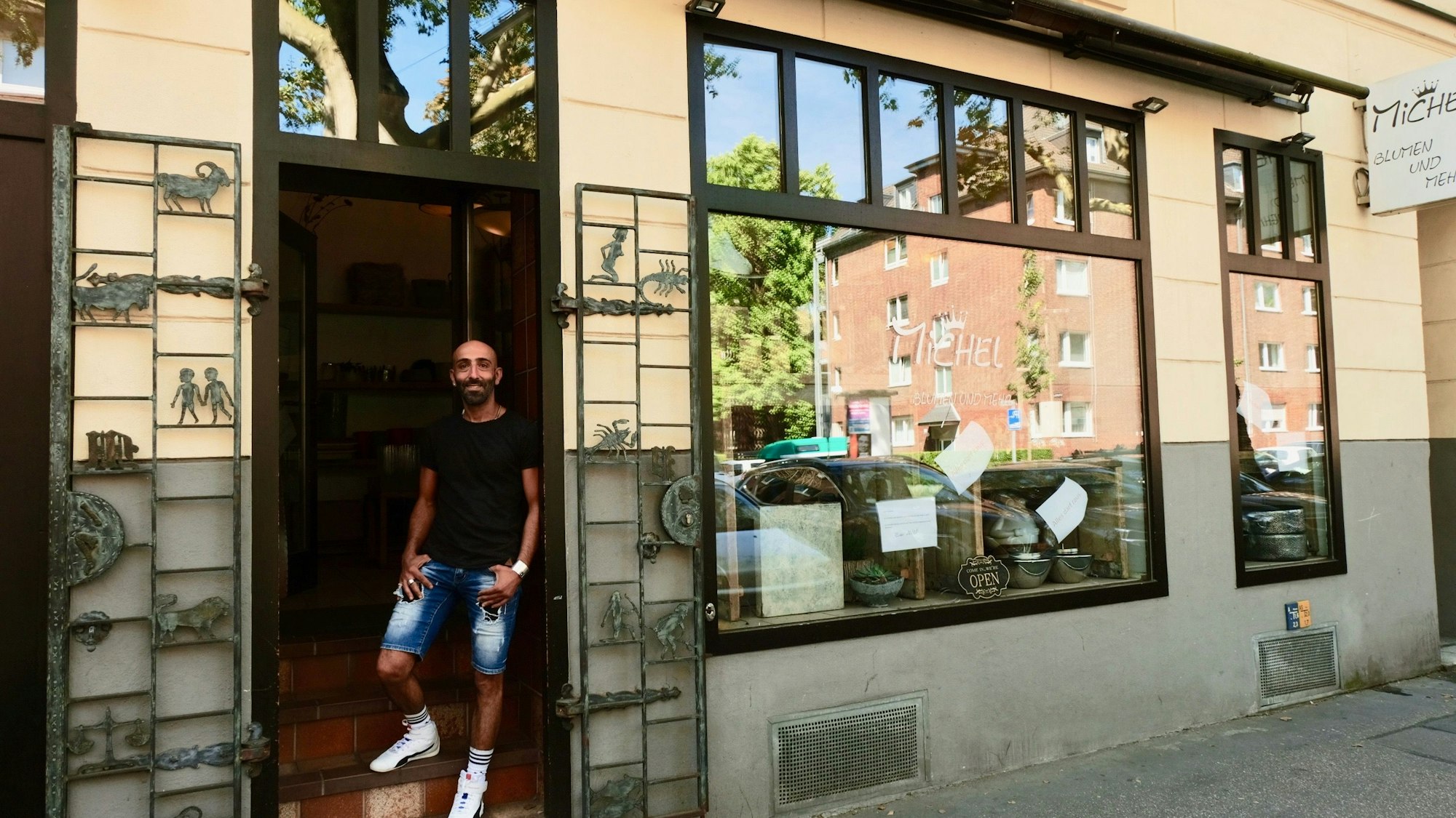 Ein Mann mit dunklem T-Shirt und kurzer Jeans steht im Eingang eines Ladenlokals.