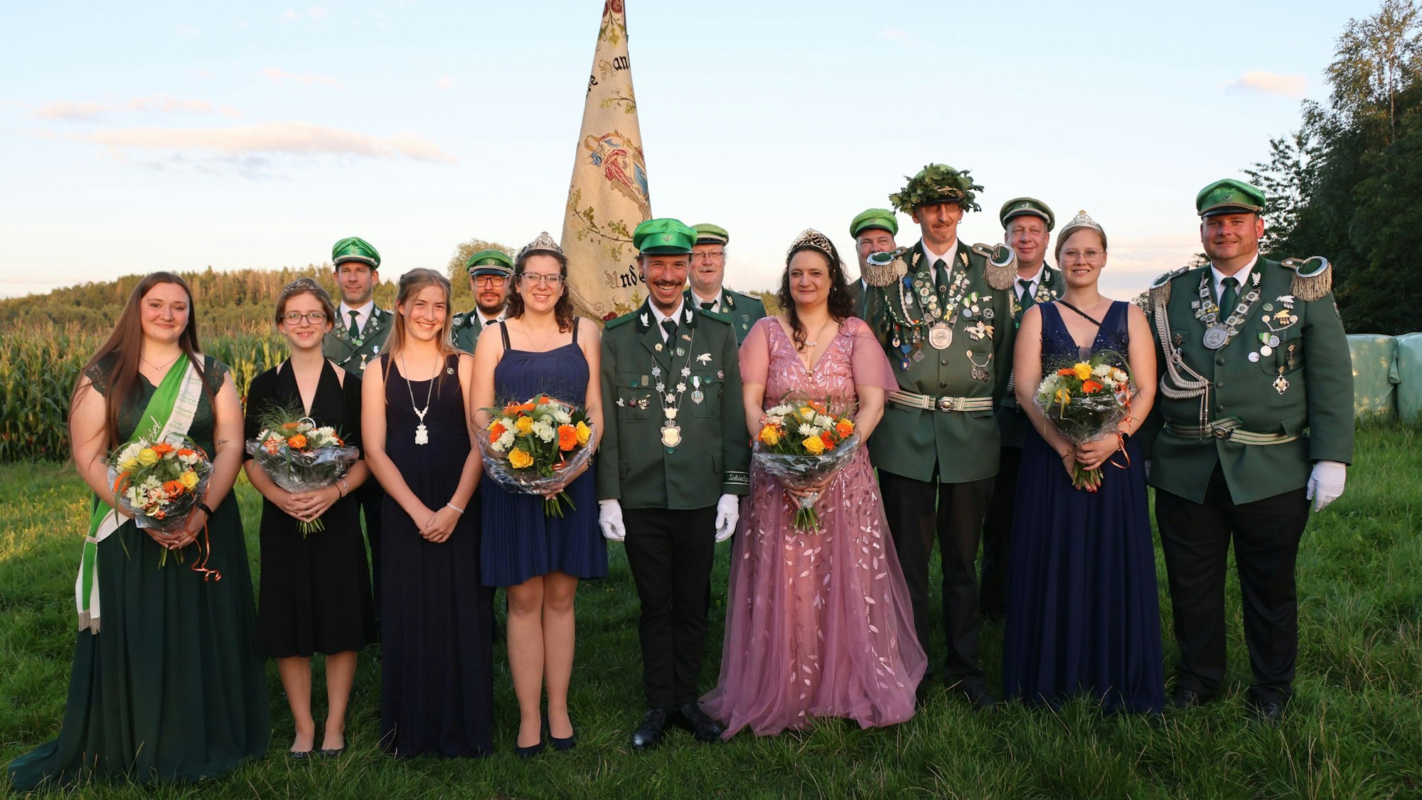 Mehrere Schützen in Uniform und Frauen in Ballkleidern stehen als Gruppe auf einer Wiese zusammen. Im Hintergrund ist die Fahre der Schützen aus Lieberhausen zu sehen.