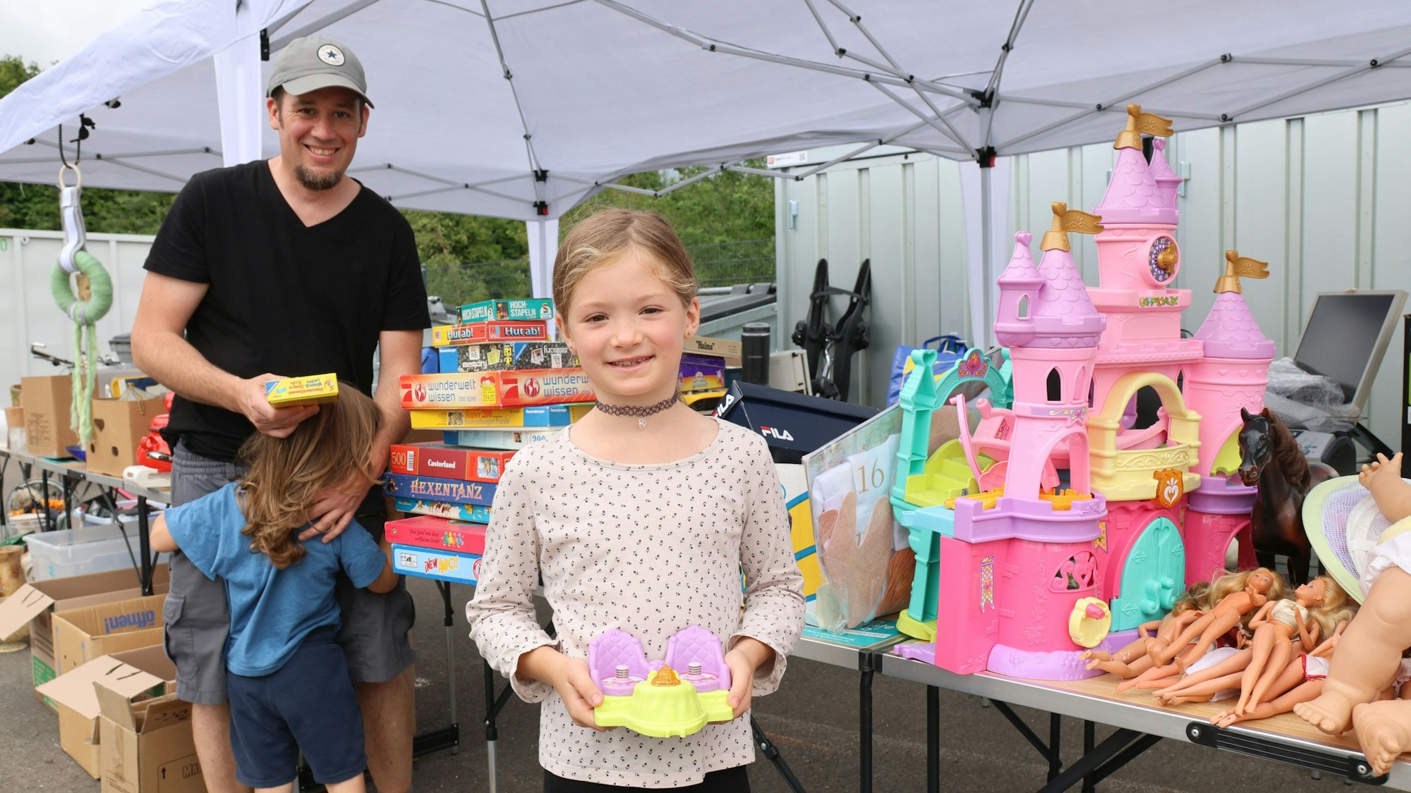 Ein siebenjähriges Mädchen steht neben Vater und kleinem Bruder und zeigt ein Plastikspielzeug.