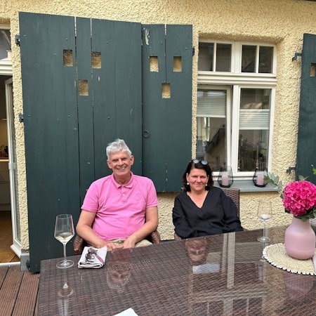 Ein Paar sitzt auf einer Dachterrasse an einem Holztisch.