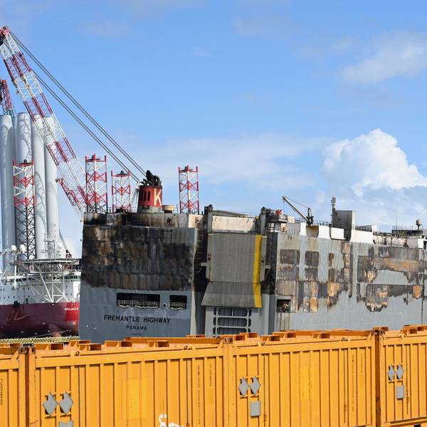 Der schwer beschädigte Frachter „Fremantle Highway“ liegt im Hafen von Eemshaven an der niederländischen Nordseeküste. Sie wird von einem Notfallschlepper gestützt. Davor sind gelbe Container aufgebaut.