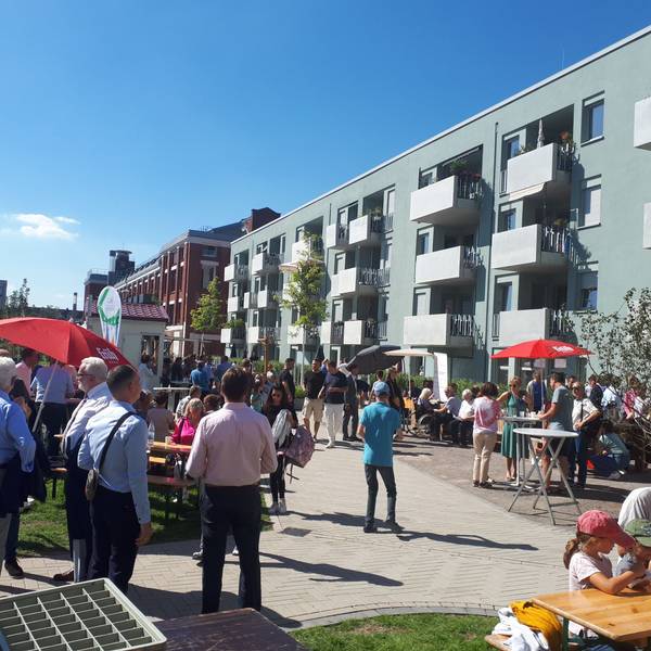 Mehrere Menschen stehen vor dem neuen Wohnhaus an der Ecke Josefine-Clouth-Straße/Xantener Straße.