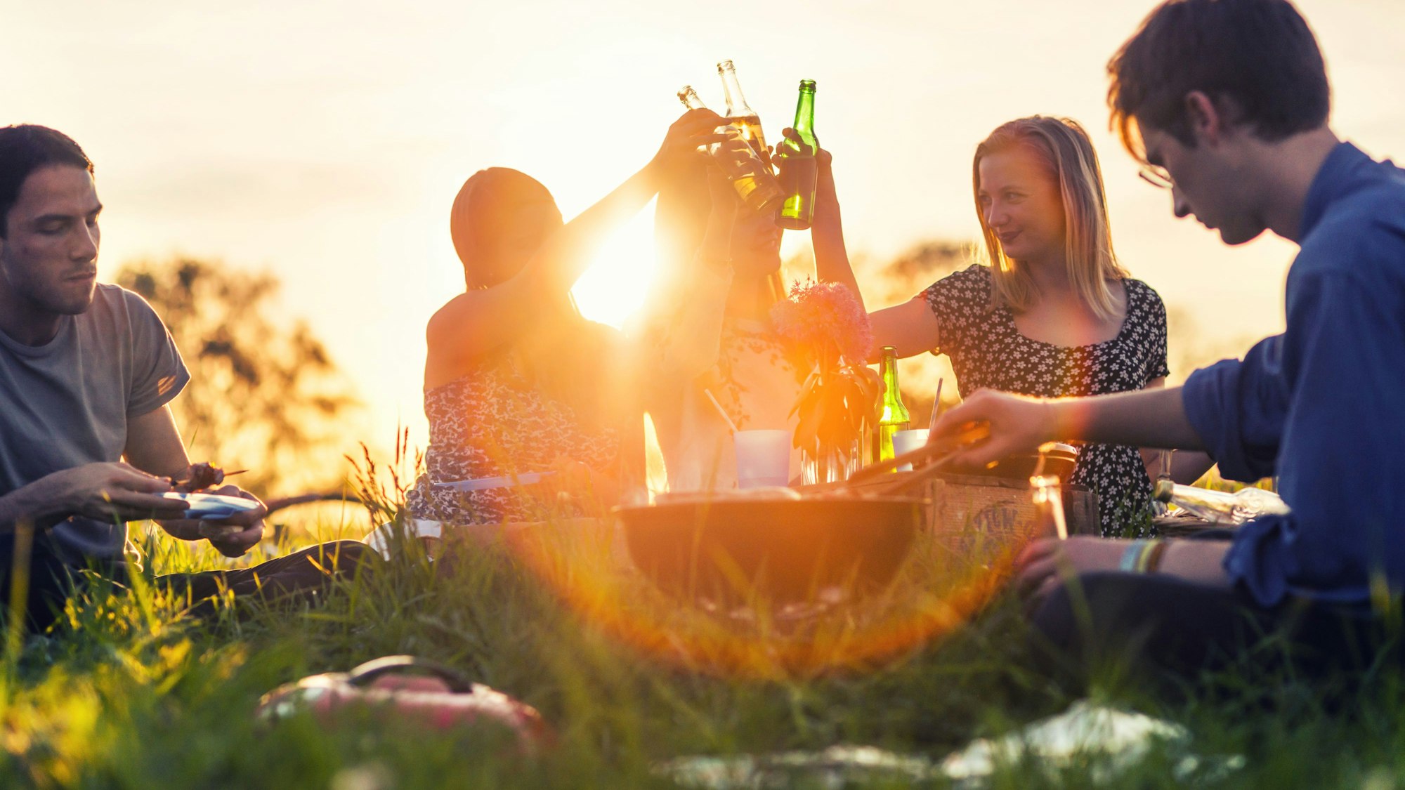 Freunde stoßen mit Flaschen an und machen ein Picknick auf der Wiese.