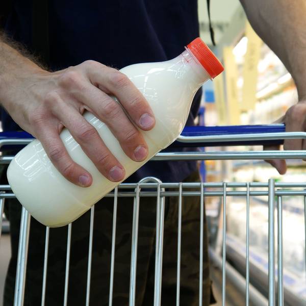 Nahaufnahme einer männlichen Käuferhand, die eine Plastikflasche Milch in einen Einkaufswagen legt.