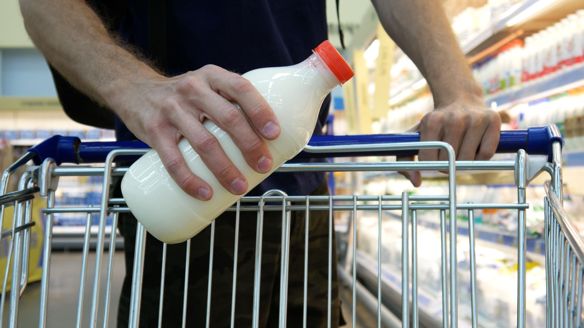 Nahaufnahme einer männlichen Käuferhand, die eine Plastikflasche Milch in einen Einkaufswagen legt.