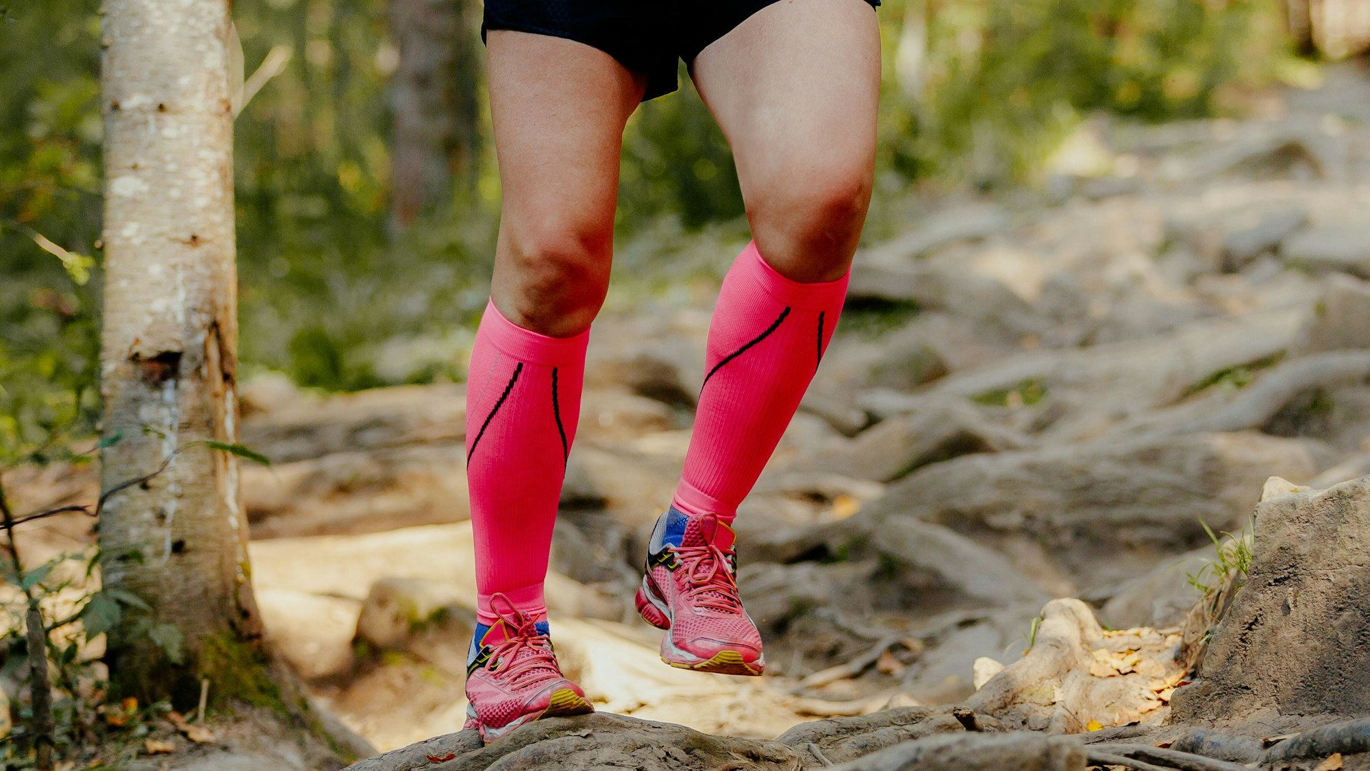 Eine Person trägt pinkfarbene Kompressionsstrümpfe mit eingenähten Reflektorstreifen beim Laufen.