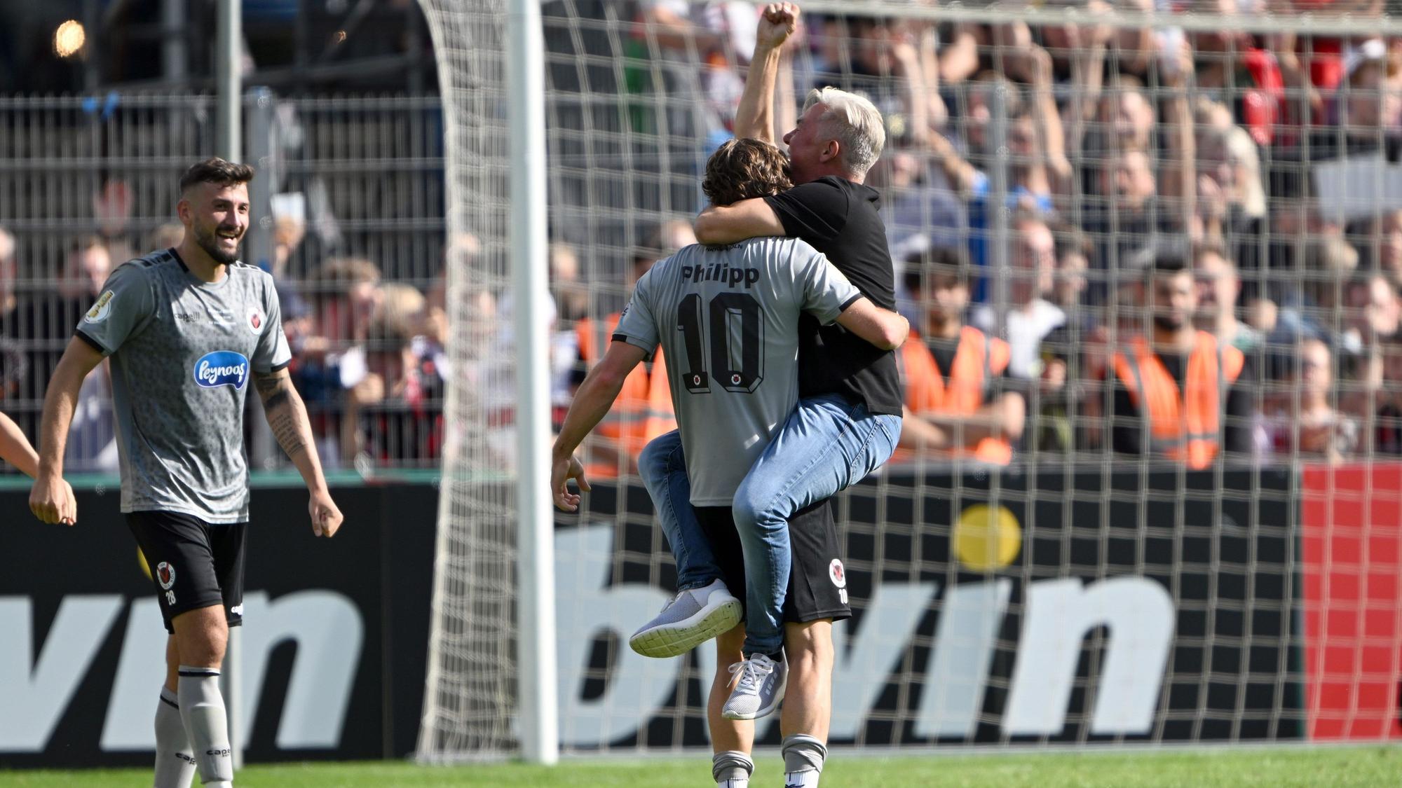 12.08.2023, Nordrhein-Westfalen, Köln: Fußball: DFB-Pokal, Viktoria Köln - Werder Bremen, 1. Runde, Sportanlage Höhenberg. Kölns David Philipp (l) und sein Trainer Olaf Janßen feiern den 3:2-Sieg über Werder Bremen. Foto: Federico Gambarini/dpa - WICHTIGER HINWEIS: Gemäß den Vorgaben der DFL Deutsche Fußball Liga bzw. des DFB Deutscher Fußball-Bund ist es untersagt, in dem Stadion und/oder vom Spiel angefertigte Fotoaufnahmen in Form von Sequenzbildern und/oder videoähnlichen Fotostrecken zu verwerten bzw. verwerten zu lassen. +++ dpa-Bildfunk +++
