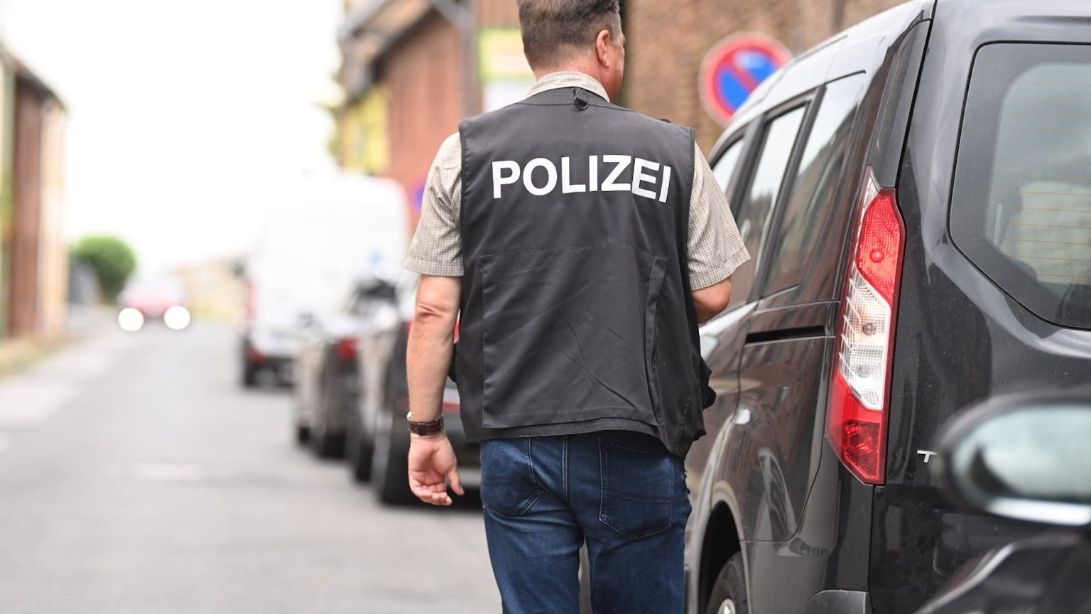 Ein Polizist steht auf einer Dorfstraße neben einem Auto.