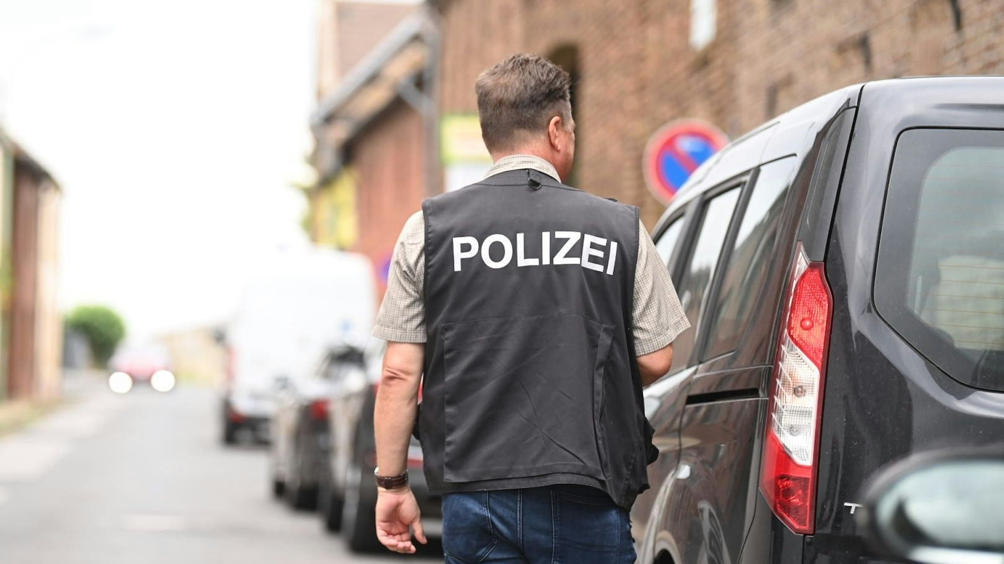 Ein Polizist steht auf einer Dorfstraße neben einem Auto.