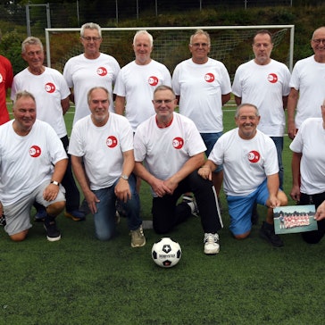 Eine Fußballmannschaft, bestehend aus alten Herren, posiert zum Mannschaftsfoto auf einem Rasenplatz.