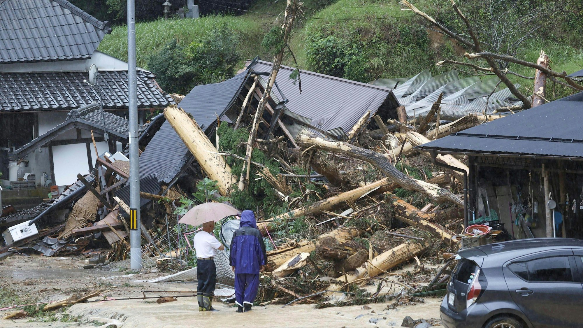 Menschen stehen nach einem Sturm an einem zerstörten Haus. Der Taifun „Lan“ ist in Japan auf Land getroffen.