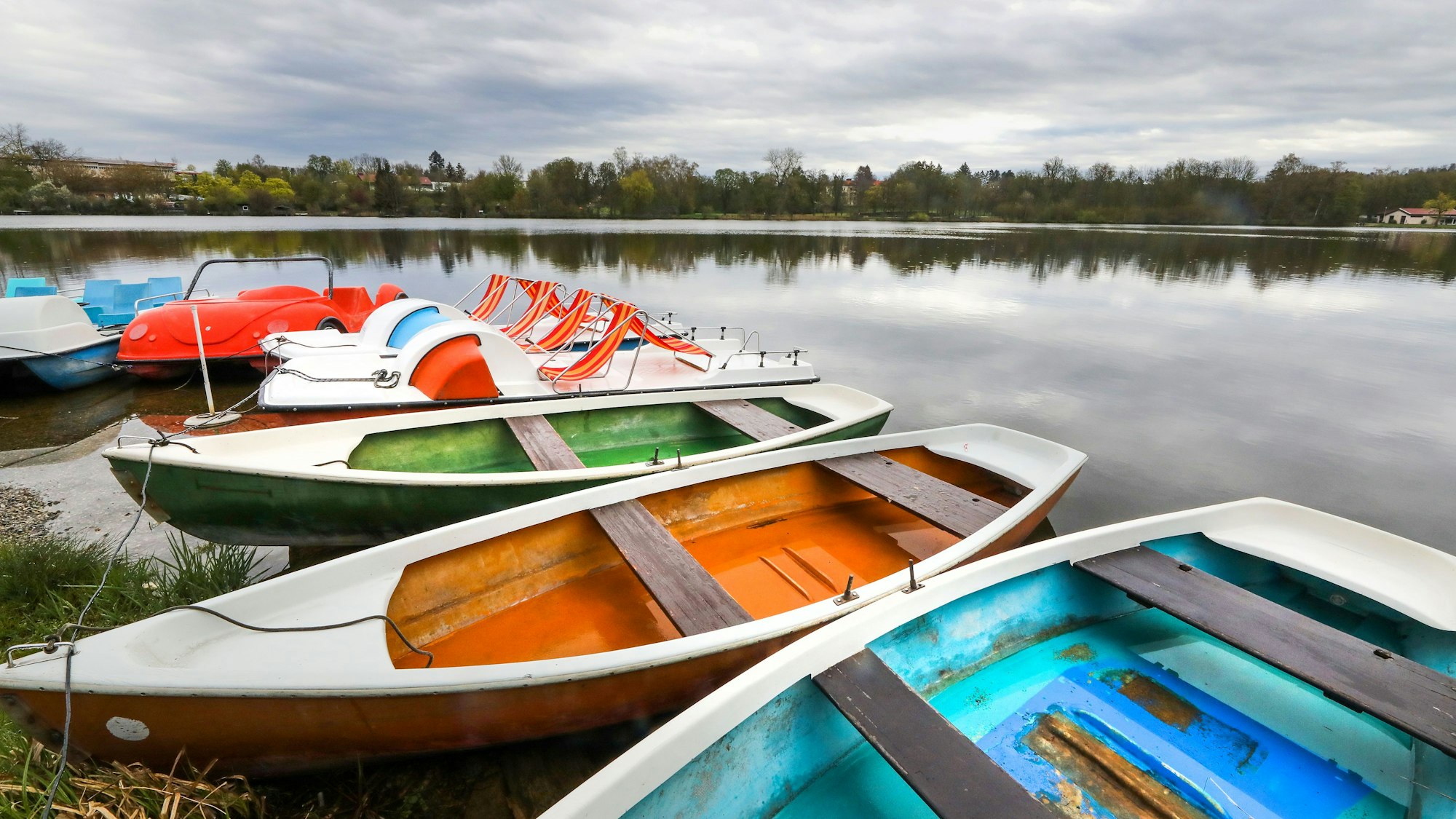Bunte Boote, unter anderem auch Tretboote, liegen am Ufer eines Sees im Wasser (Symbolbild). In Tirol hat ein Österreicher ein solches Boot als Waffe eingesetzt.