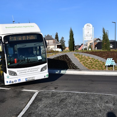 Ein weißer Linienbus fährt in einem Kreisverkehr.