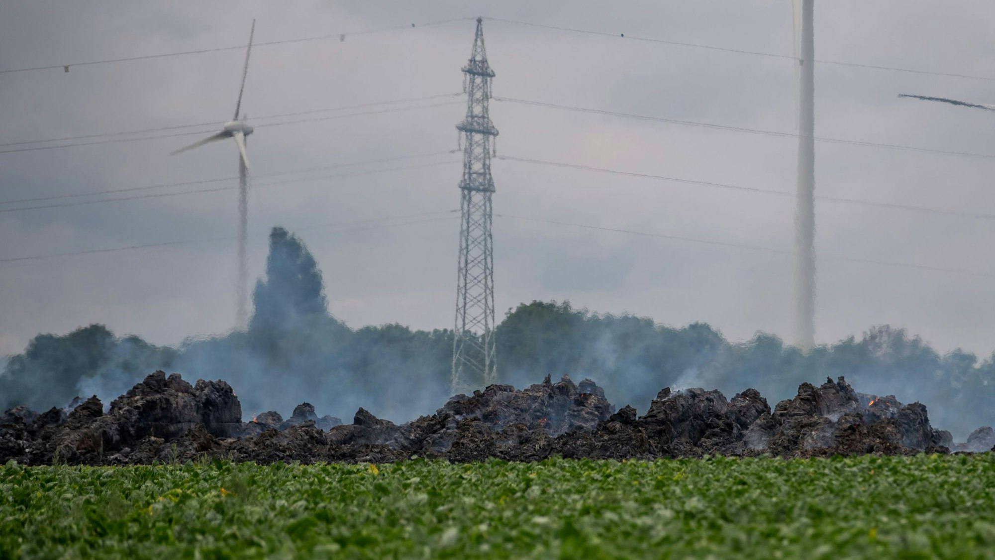 Das Bild zeigt die qualmenden Strohballen. Im Hintergrund dreht sich ein Windrad an der Autobahn.