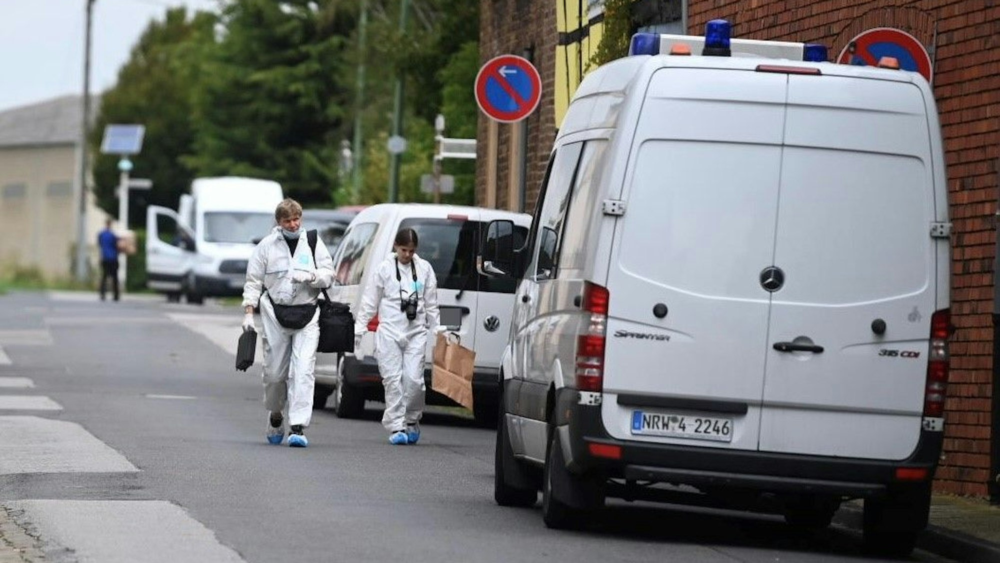 Ermittler der Polizei in weißen Schutzanzügen gehen eine Straße entlang.