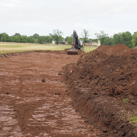 Ein Bagger hat Erde auf einem Feld abgetragen und zu einem Wall aufgehäuft.
