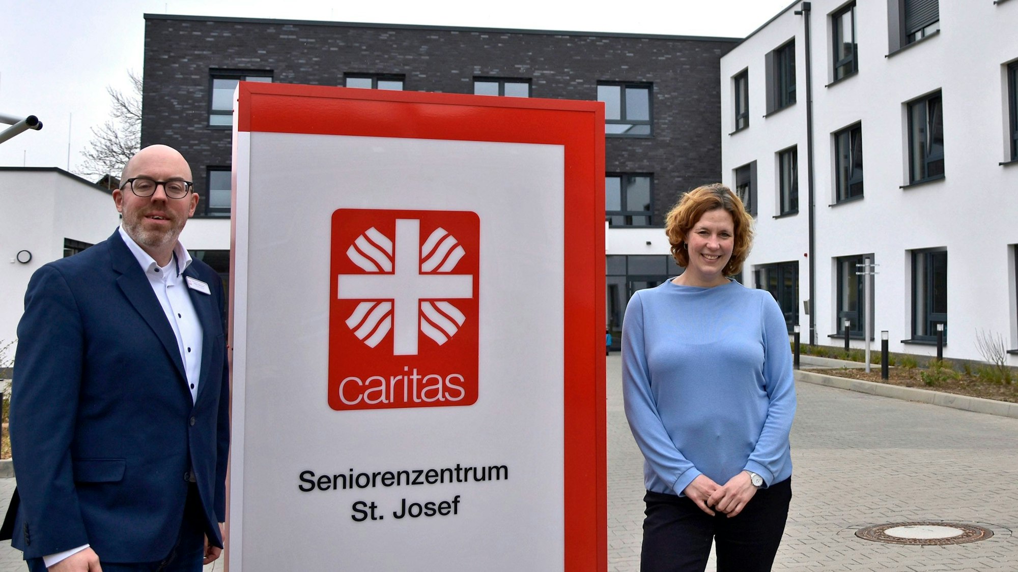 Ein Mann und eine Frau stehen neben dem Schild eines Seniorenheims.