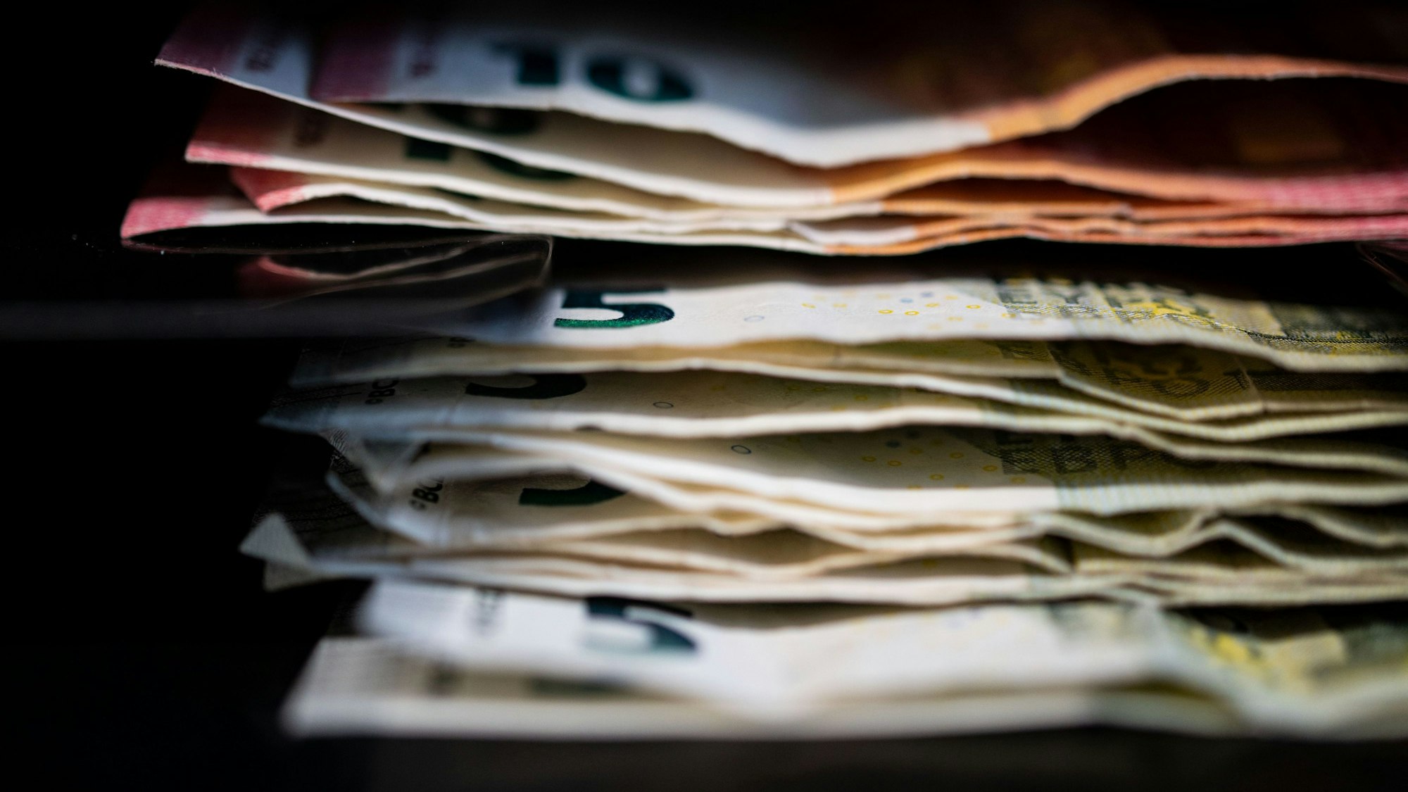 Geldscheine stapeln sich vor einem schwarzen Hintergrund. (Symbolbild)