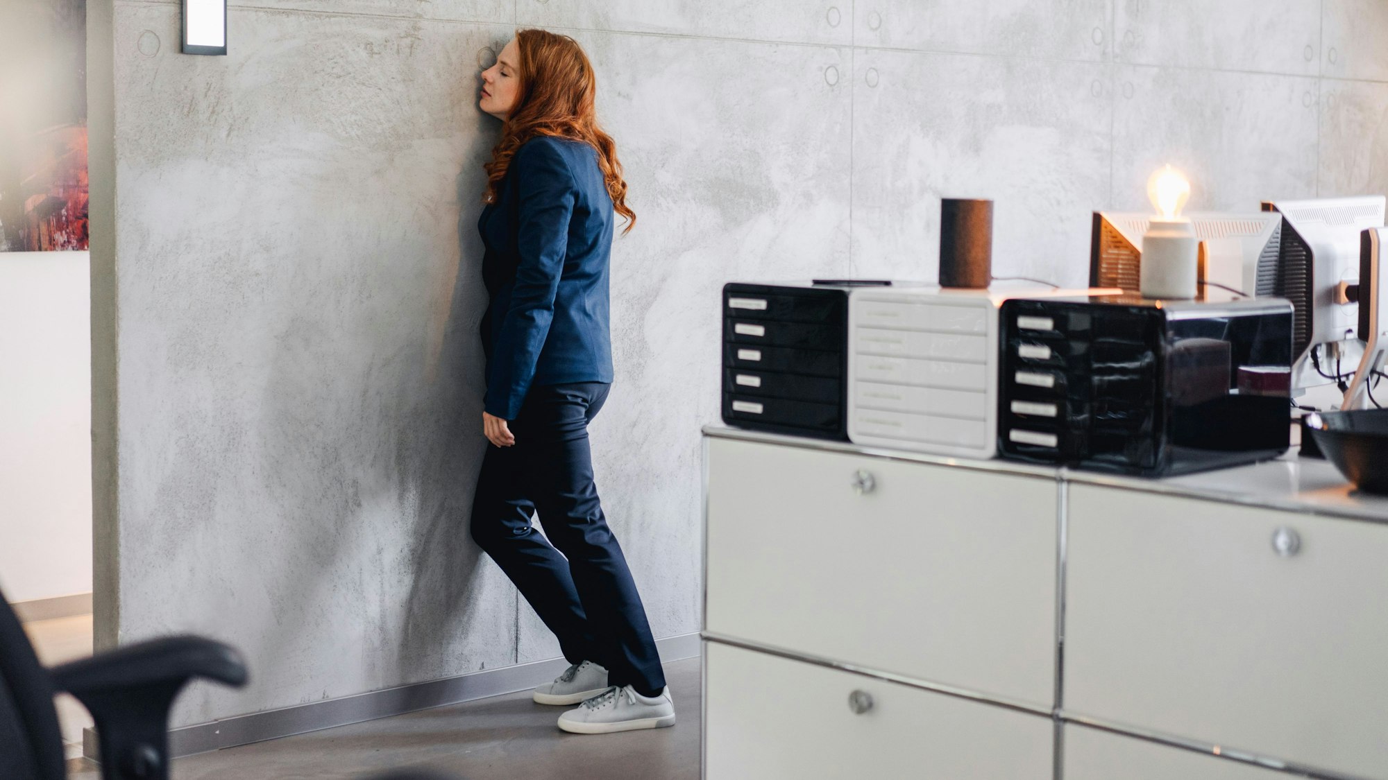 Eine Frau lehnt erschöpft an der Wand ihres Büros.