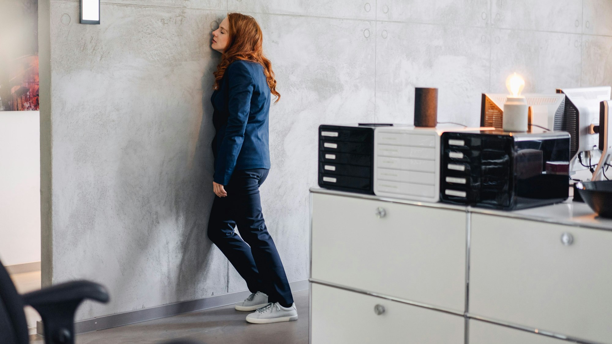 Eine Frau lehnt erschöpft an der Wand ihres Büros.