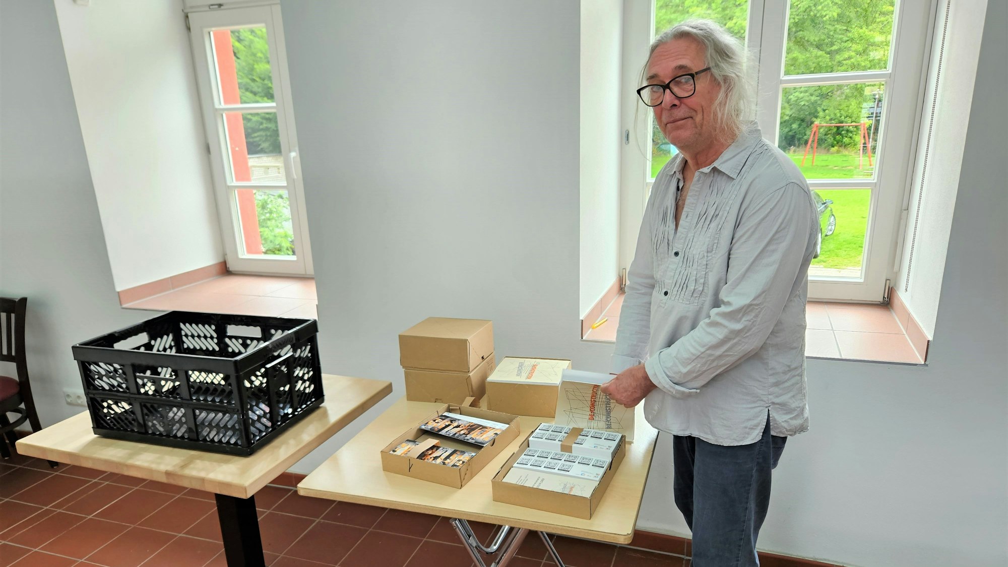 Der Künstler Jürgen A. Roder steht an einem Tisch mit Infomaterial zur Ausstellung.