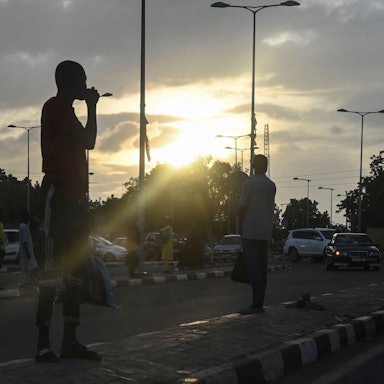 Die Umrisse von Menschen auf einer Straße in Niamey in Niger ist zu sehen - im Hintergrund bricht die Sonne durch eine dichte Wolkendecke.