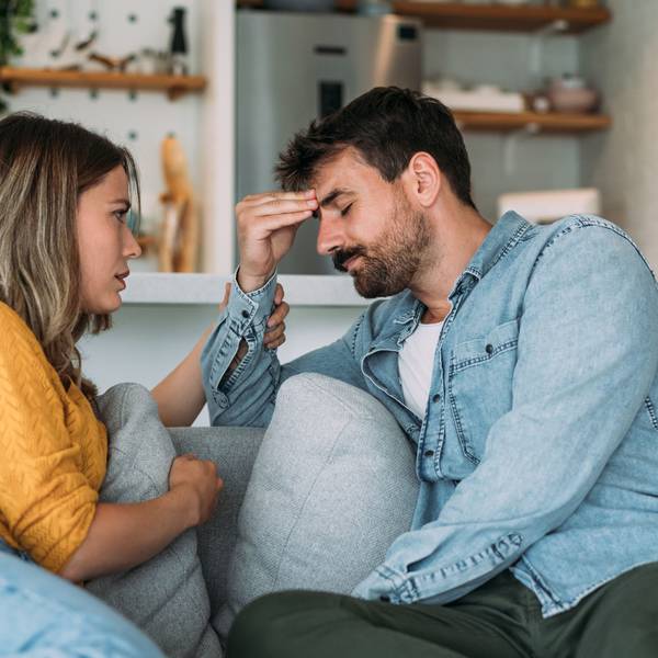 Ein junges Paar bespricht auf dem Sofa ein Problem, der Mann wirkt sehr frustriert