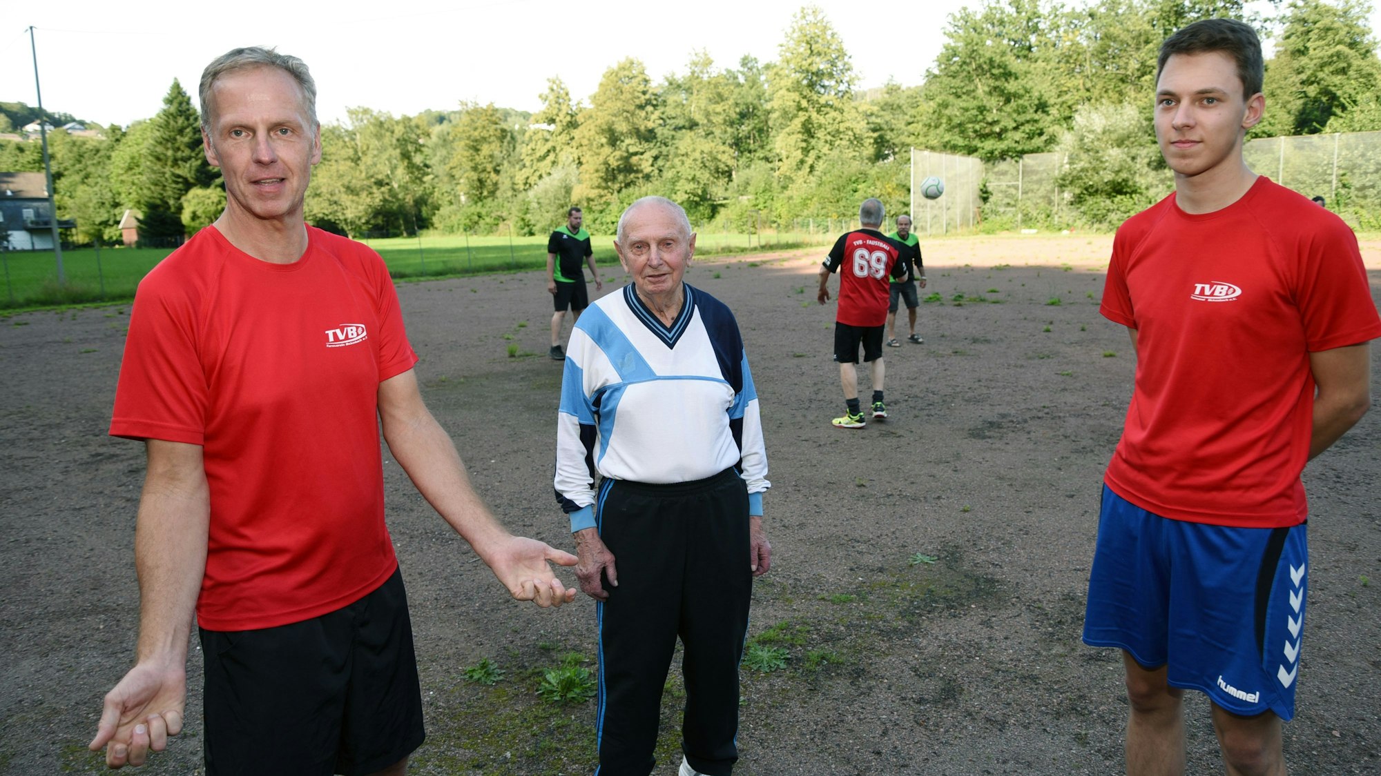 Drei Männer aus drei Familiengenerationen stehen auf einem Sportplatz nebeneinander: Vater, Sohn und Enkel.