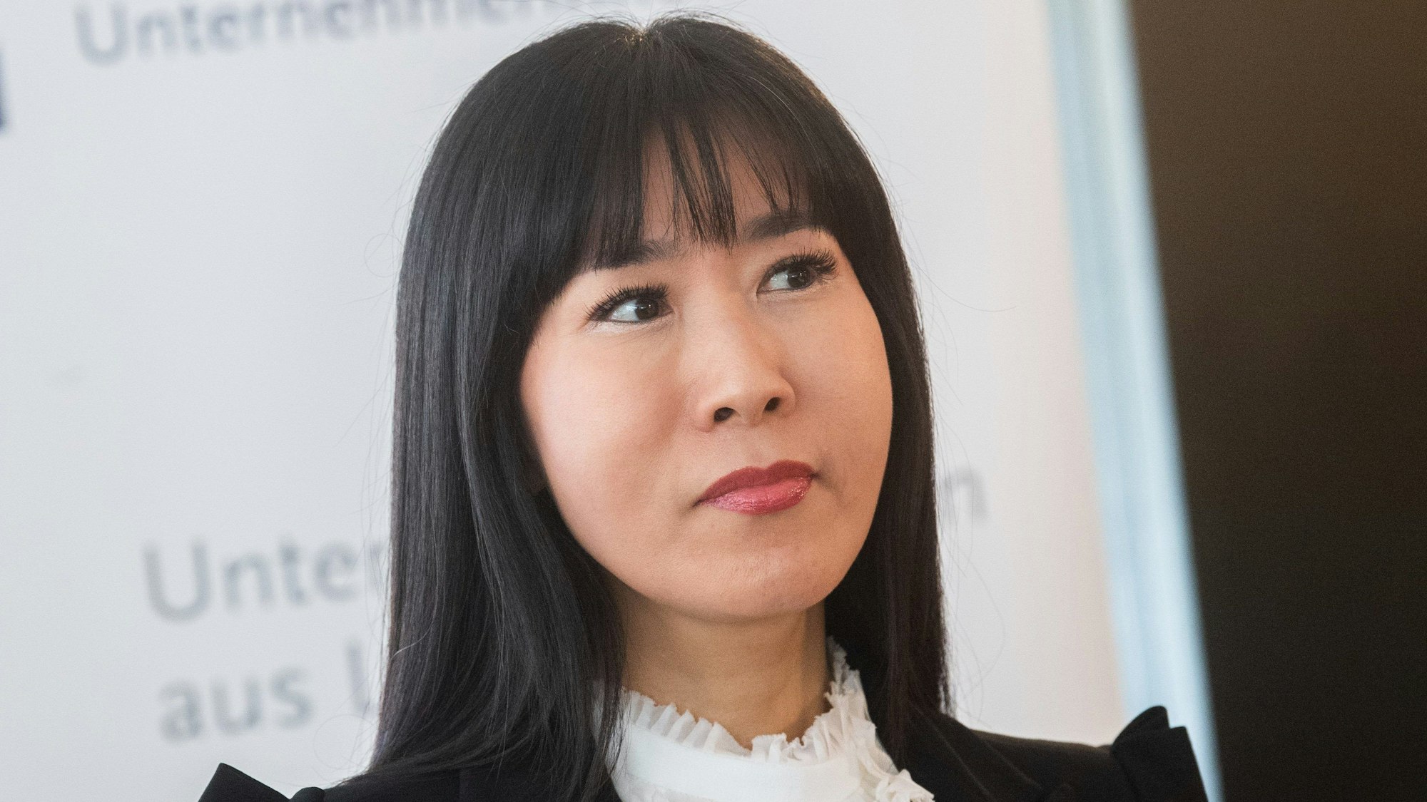 Soyeon Schröder-Kim hält einen Vortrag. Sie ist im Porträt zu sehen, trägt eine weiße Bluse und ein schwarzes Jackett.