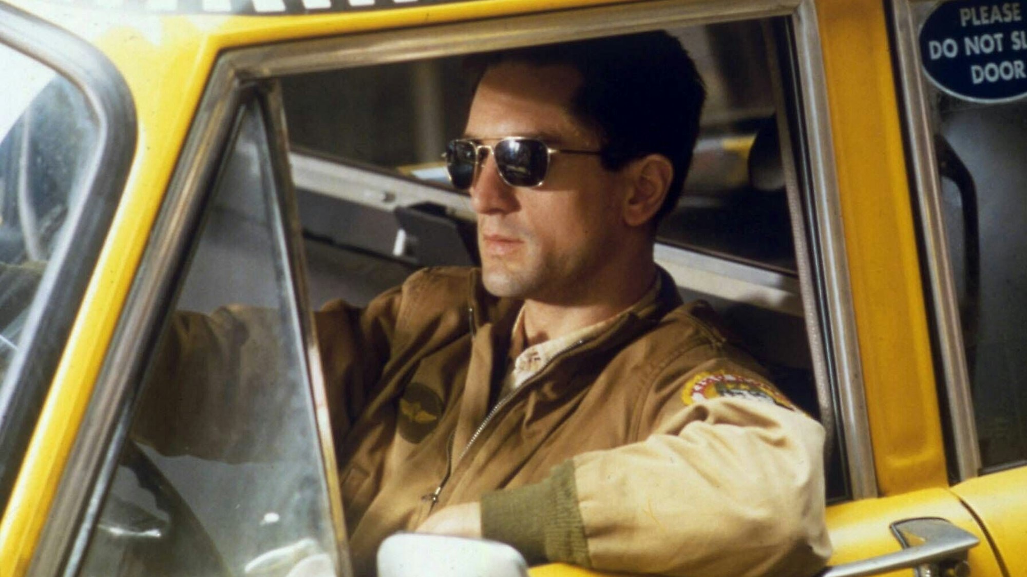 Ein Mann mit Sonnenbrille sitzt am Steuer eines Taxis.