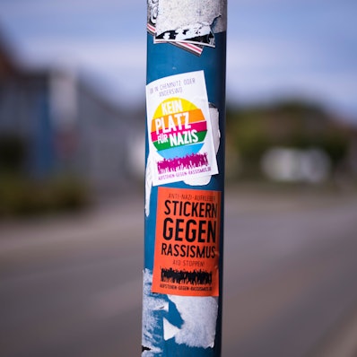 Auf einer Straßenlaterne sind Sticker gegen Nazis und Rassismus aufgeklebt.