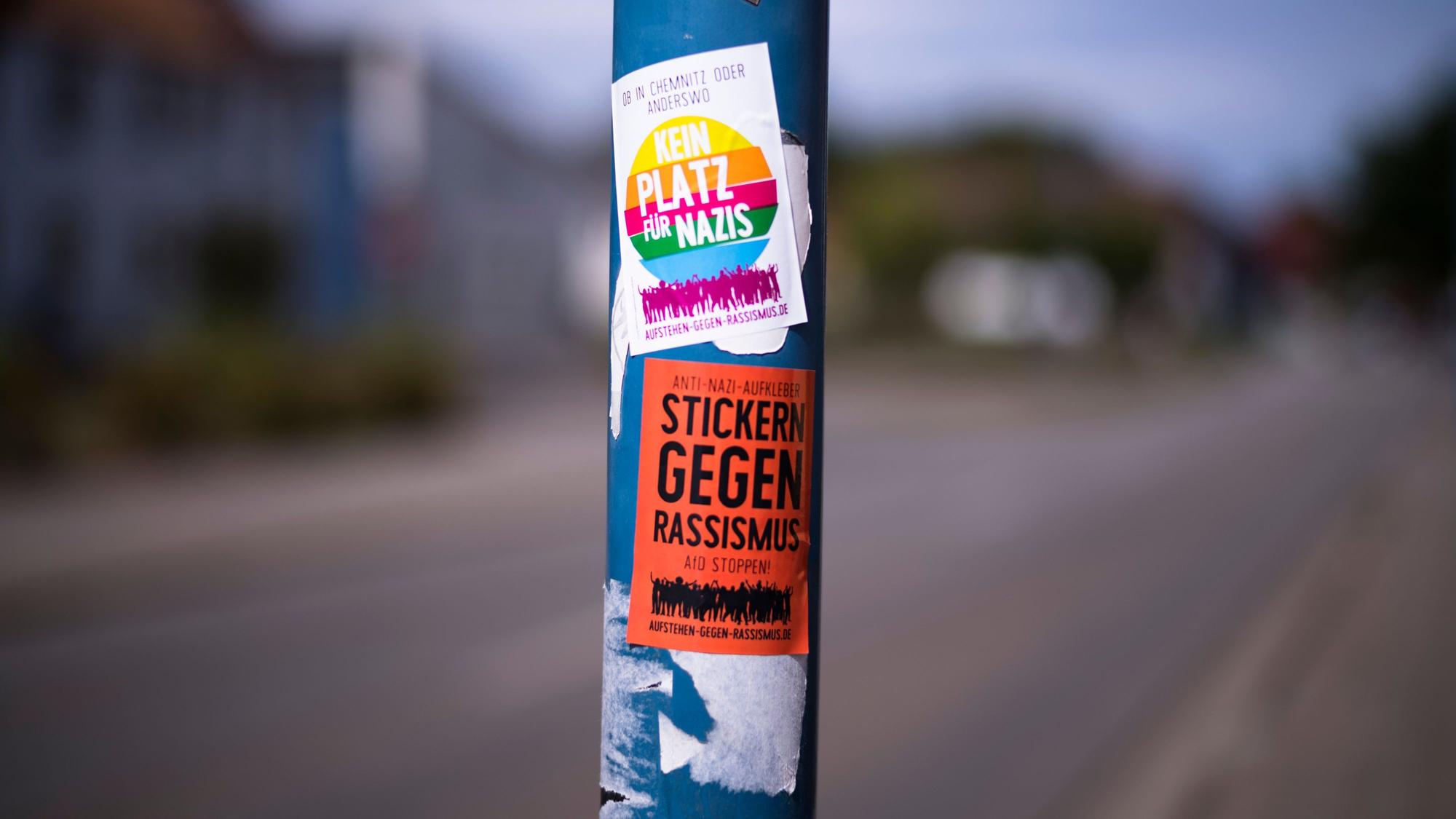 Auf einer Straßenlaterne sind Sticker gegen Nazis und Rassismus aufgeklebt.