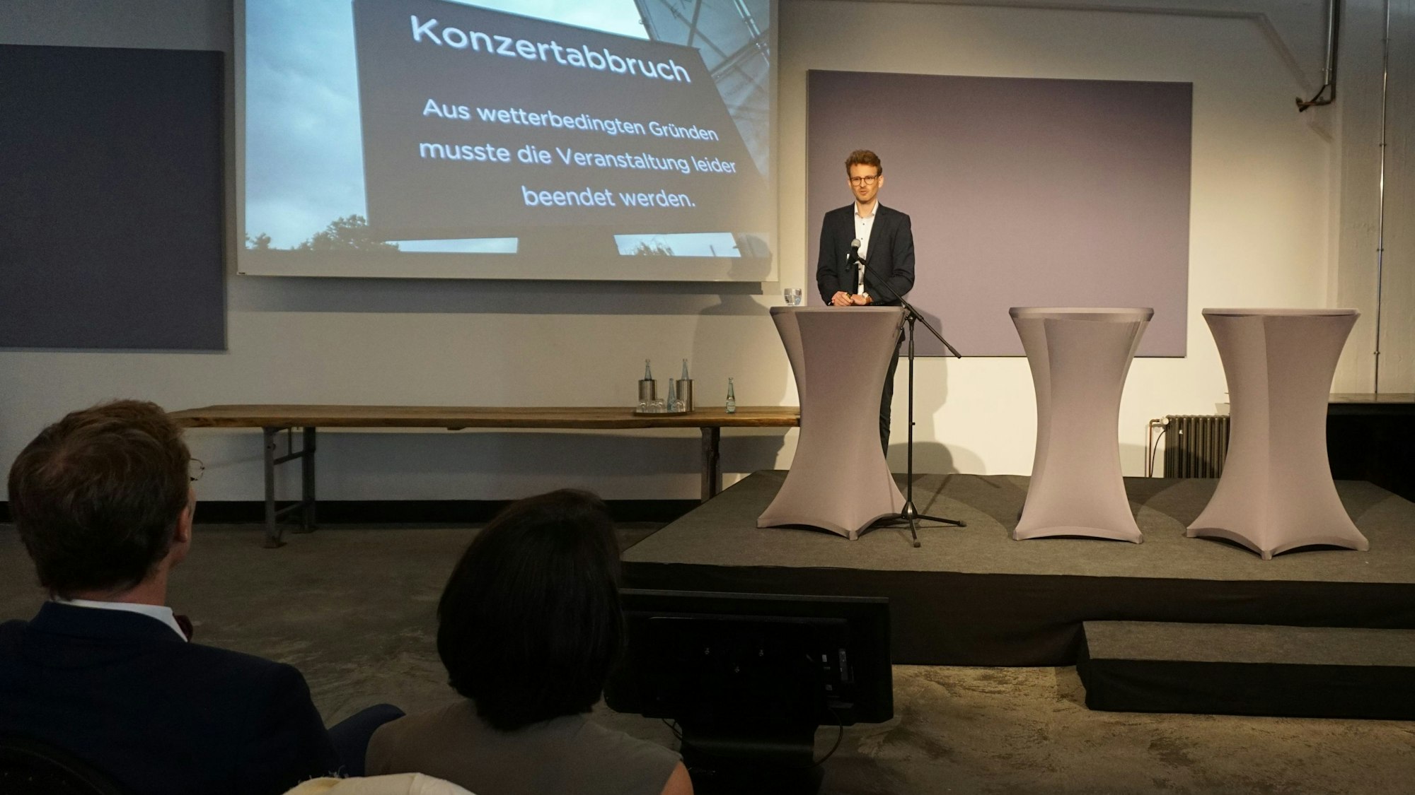 Freizeit- und Tourismusberater Lukas Melzer steht an einem Rednerpult. Auf die Wand wird ein Foto projiziert. Es hat die Aufschrift: „Konzertabbruch – Aus wetterbedingten Gründen musste die Veranstaltung leider beendet werden“.