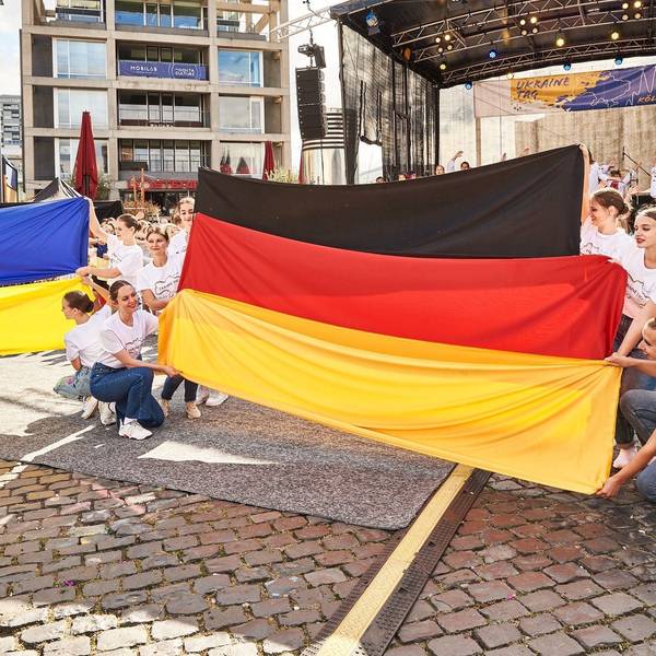 Junge Frauen halten beim Ukraine Tag 2022 vor einer Bühne am Schokoladenmuseum die ukrainische und die deutsche Nationalfahne in den Händen.