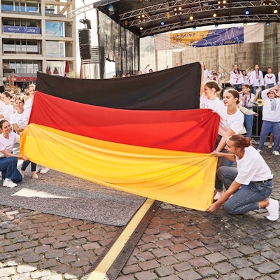 Junge Frauen halten beim Ukraine Tag 2022 vor einer Bühne am Schokoladenmuseum die ukrainische und die deutsche Nationalfahne in den Händen.