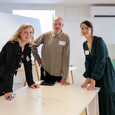 Zwei Frauen und ein Mann stehen an einem Tisch, der mit Stiften beschrieben werden kann.