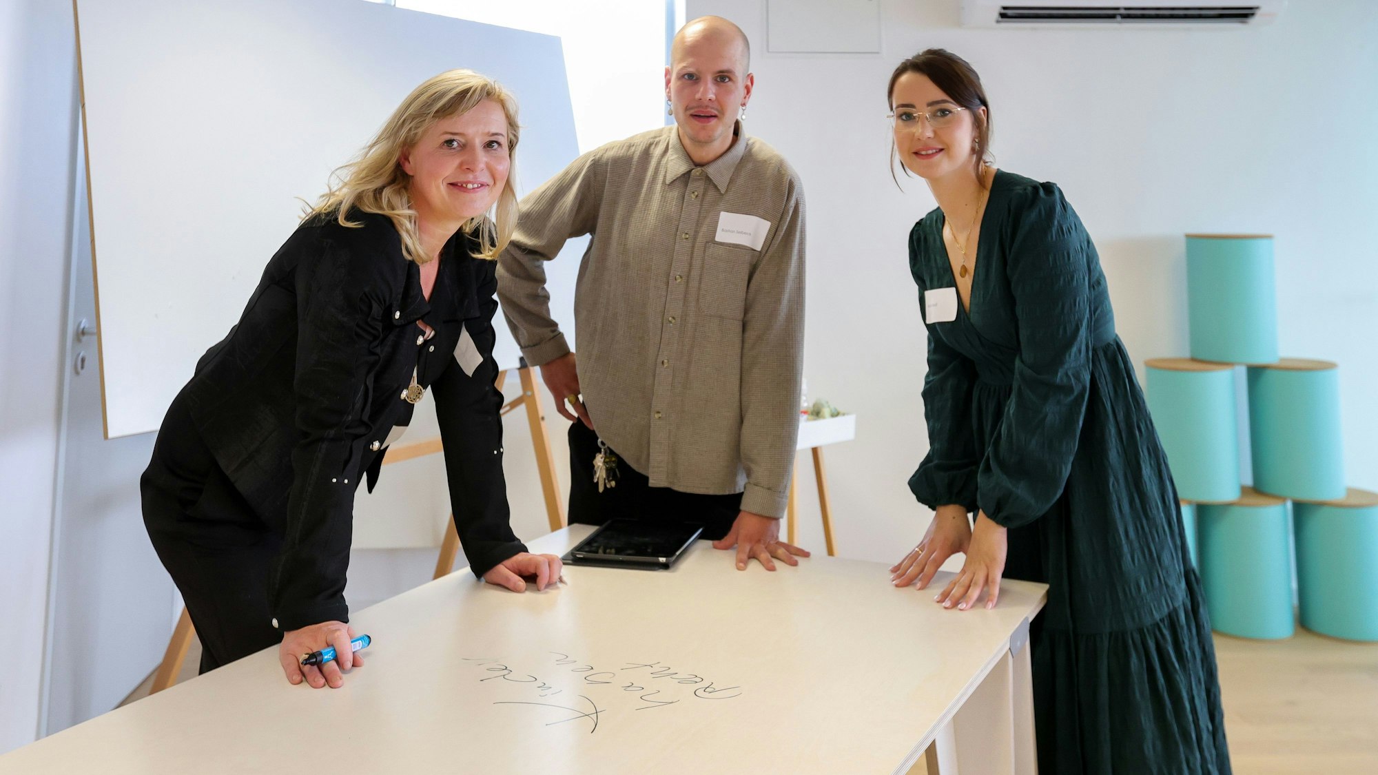 Zwei Frauen und ein Mann stehen an einem Tisch, der mit Stiften beschrieben werden kann.