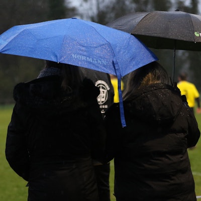 Zwei Zuschauerinnen stehen mit Regenschirm am Rande eines Fußballspiels.
