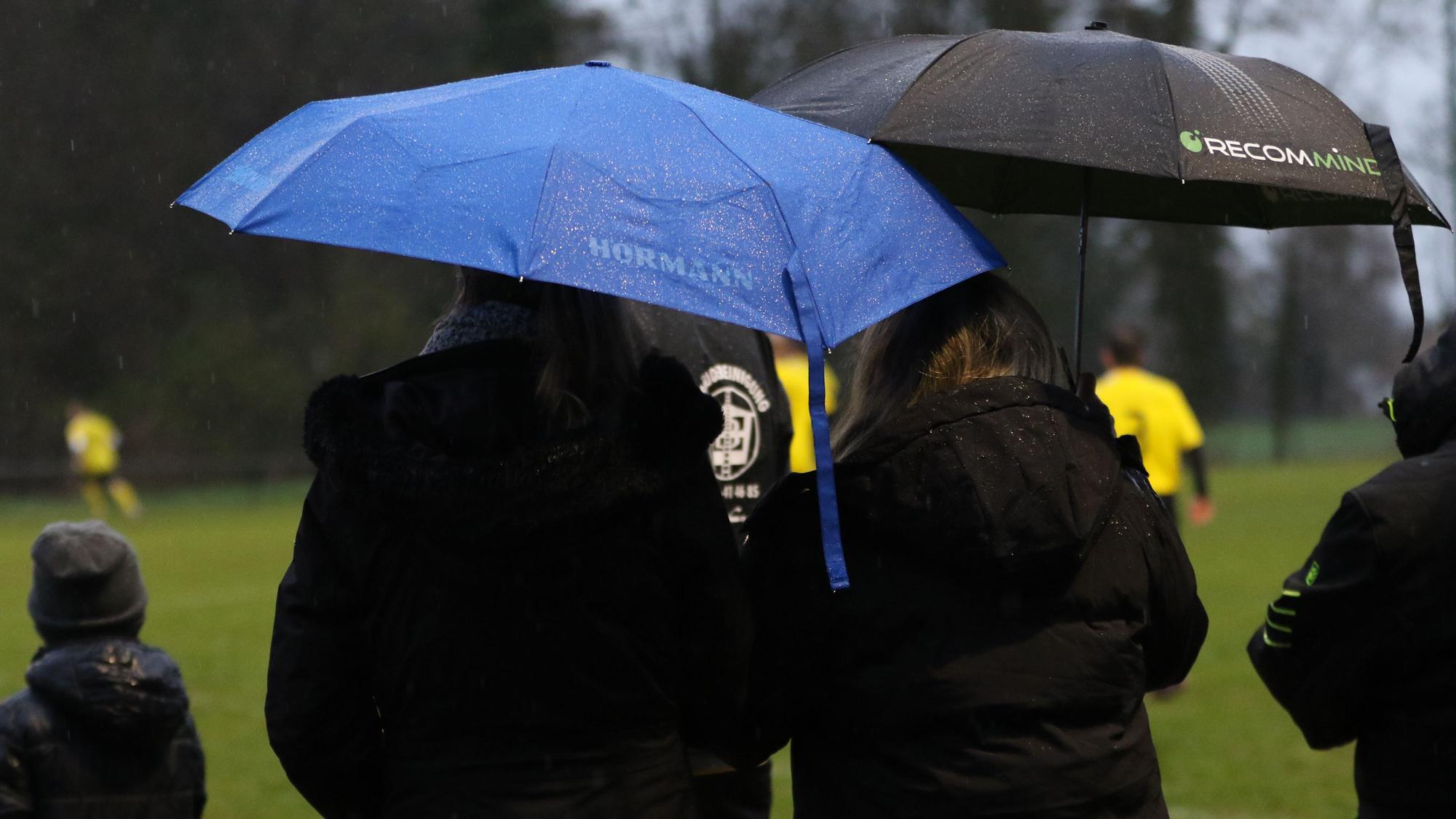 Zwei Zuschauerinnen stehen mit Regenschirm am Rande eines Fußballspiels.