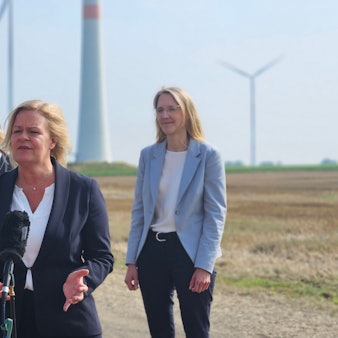 Bundesinnenministerin Nancy Faeser spricht vor Windrädern bei einem Pressetermin in Mikrophone. Hinter ihr stehen Bedburgs Bürgermeister Sascha Solbach und zwei Frauen von RWE.