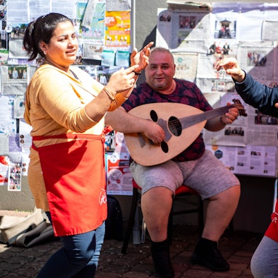Das Bild zeigt zwei Frauen, die tanzen, während ein Mann musiziert.
