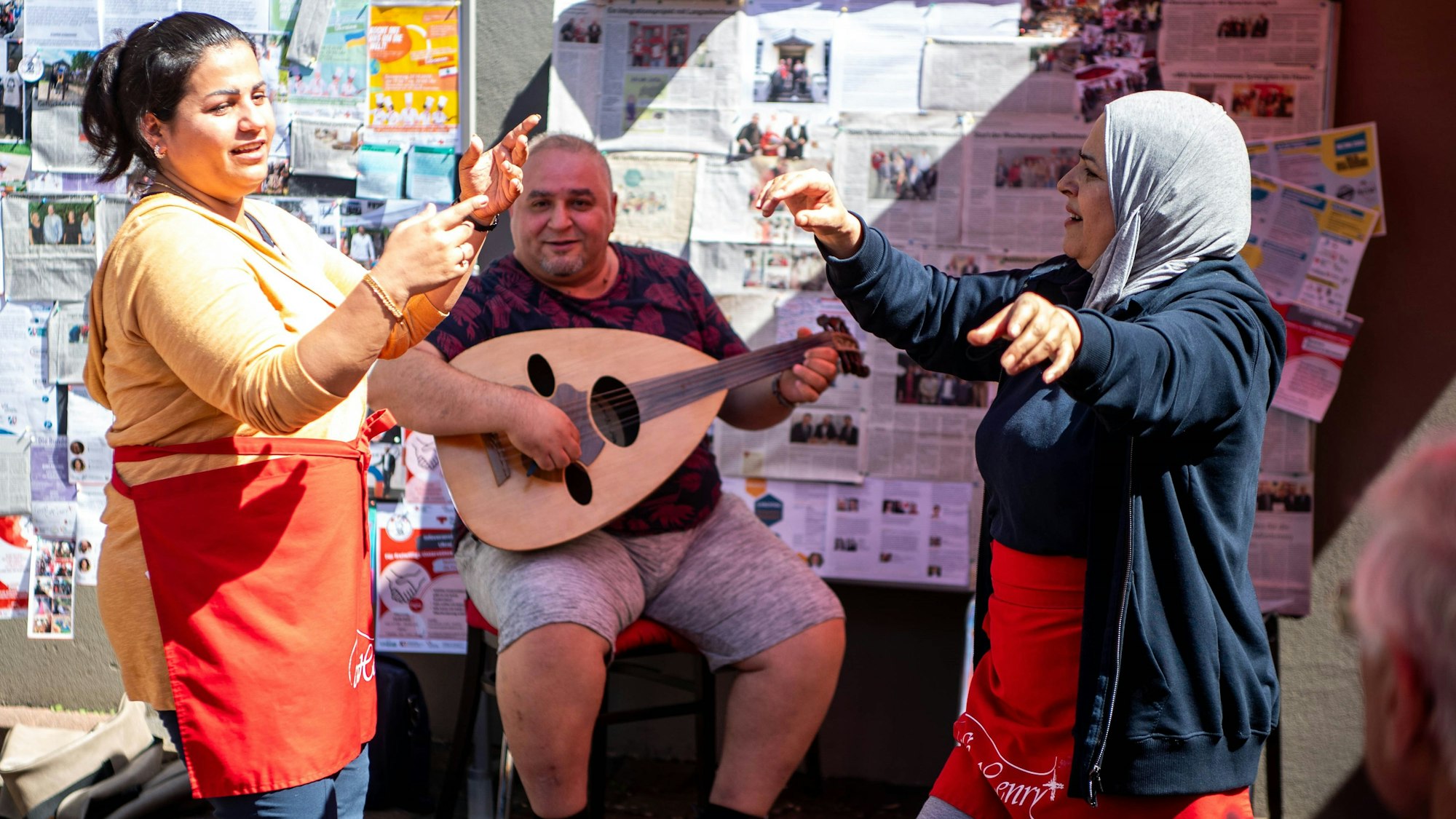 Das Bild zeigt zwei Frauen, die tanzen, während ein Mann musiziert.
