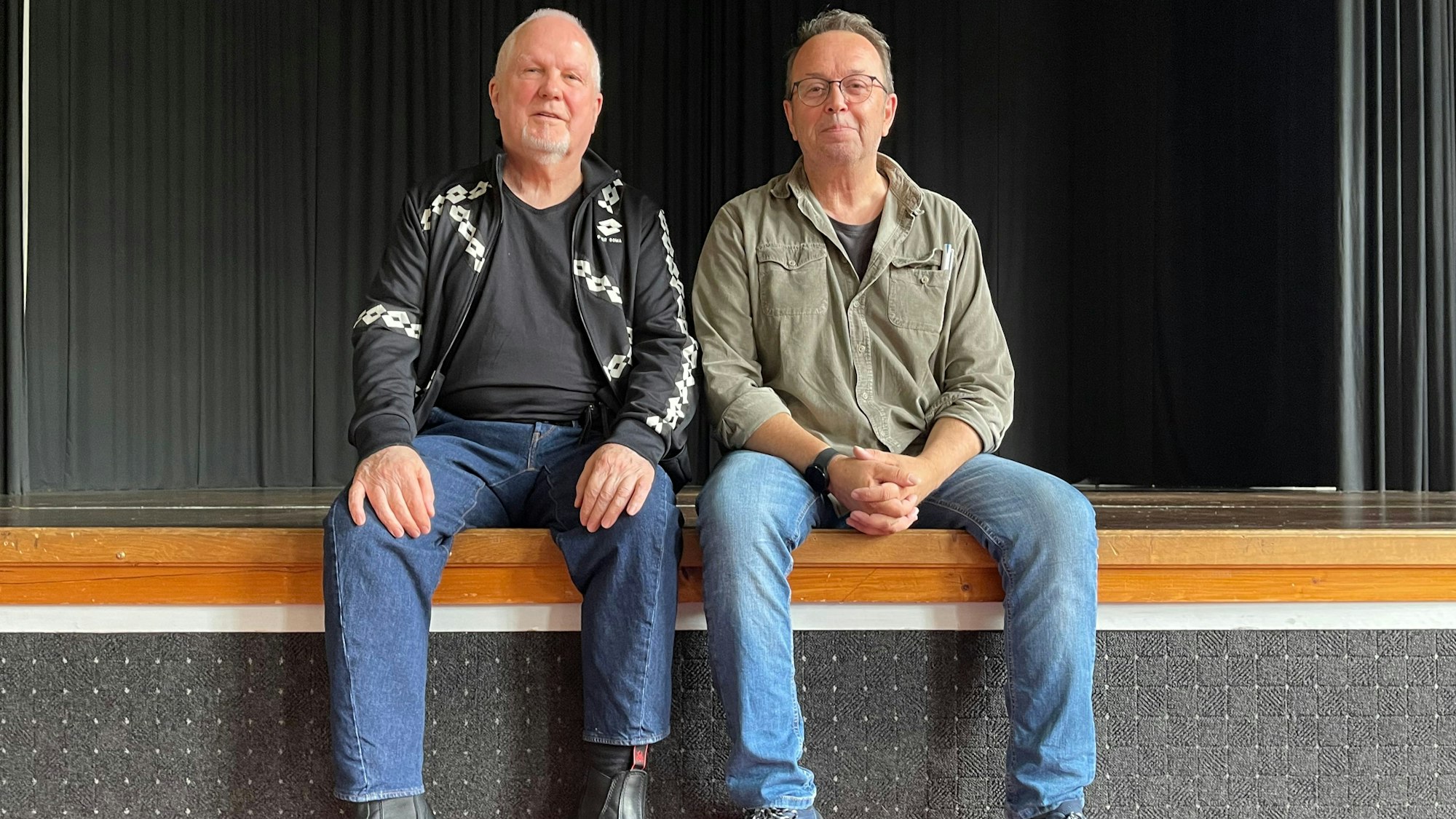 Zwei Männer sitzen auf einer Bühne.