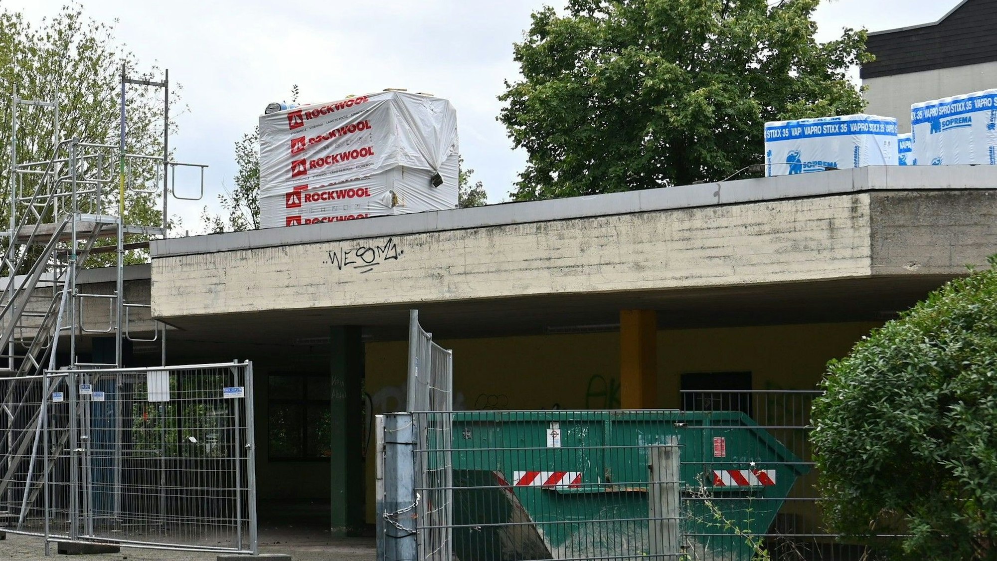 Das Dach der Gesamtschule mit Baumaterialien, vor dem Gebäude steht ein Gerüst.